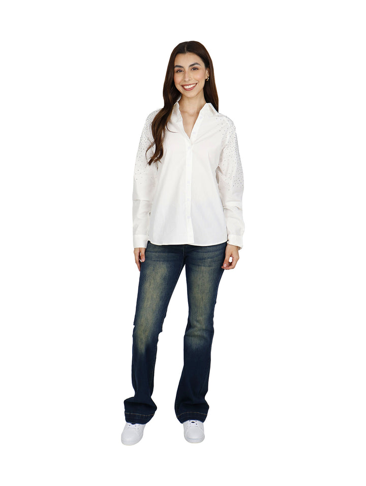 Mujer vistiendo una camisa blanca oversize de manga larga con detalles brillantes en los hombros.