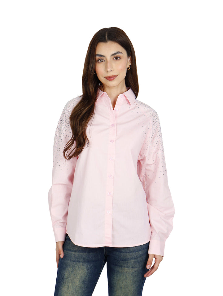 Mujer vistiendo camisa oversize color rosa claro con detalles brillantes en los hombros.