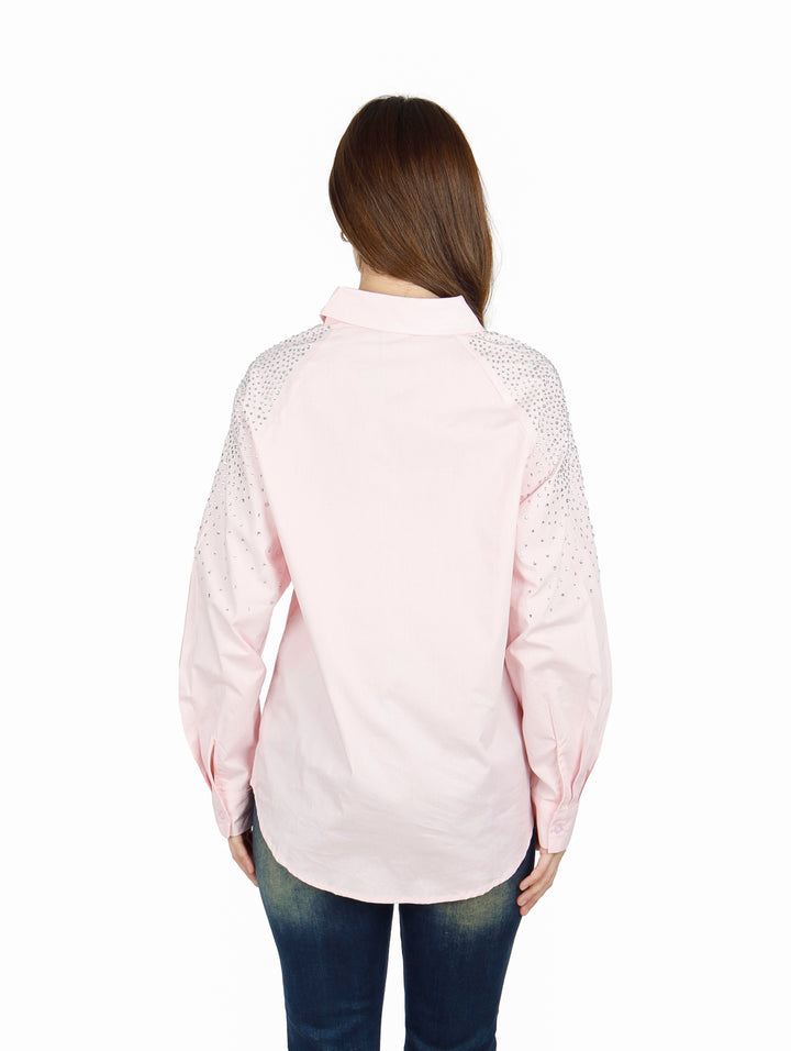 Mujer vistiendo camisa oversize color rosa claro con detalles brillantes en los hombros.