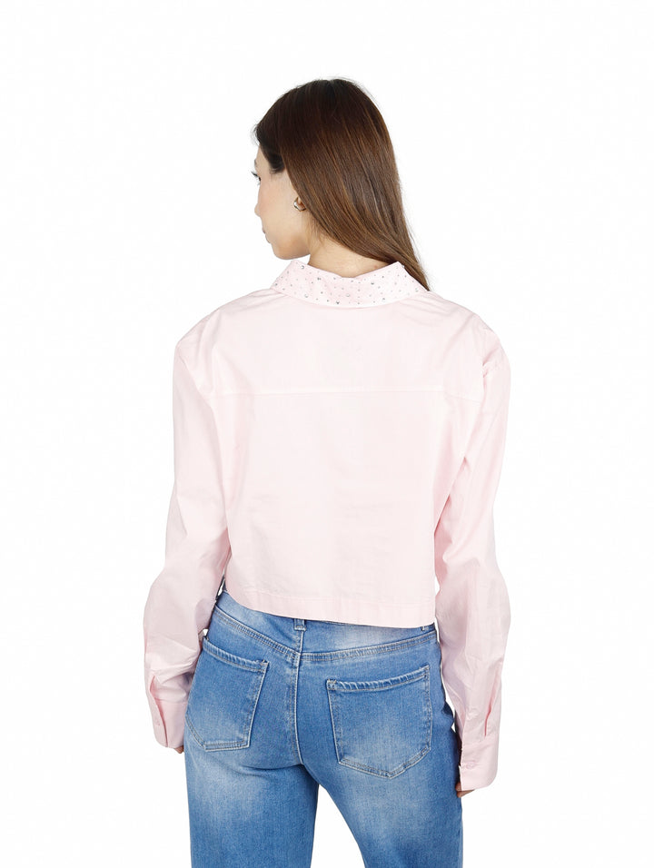 Mujer vistiendo una camisa cropped de color rosa claro con cuello y manga larga.