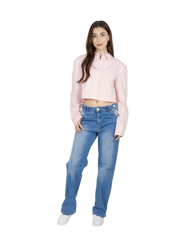 Mujer vistiendo una camisa cropped de color rosa claro con cuello y manga larga.
