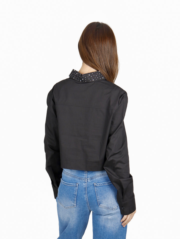 Mujer vistiendo una camisa corta negra de manga larga con cuello de lunares blancos y jeans azules.