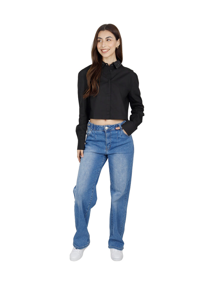 Mujer vistiendo una camisa corta negra de manga larga con cuello de lunares blancos y jeans azules.