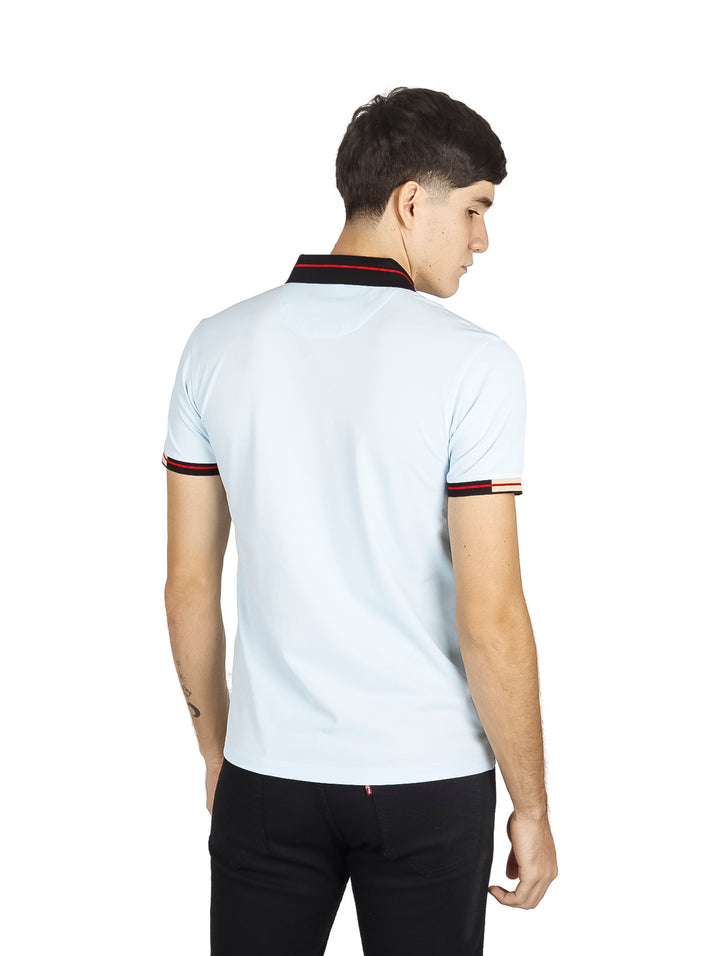 Hombre vistiendo playera polo color azul cielo con detalles negros y rojos en el cuello y mangas.