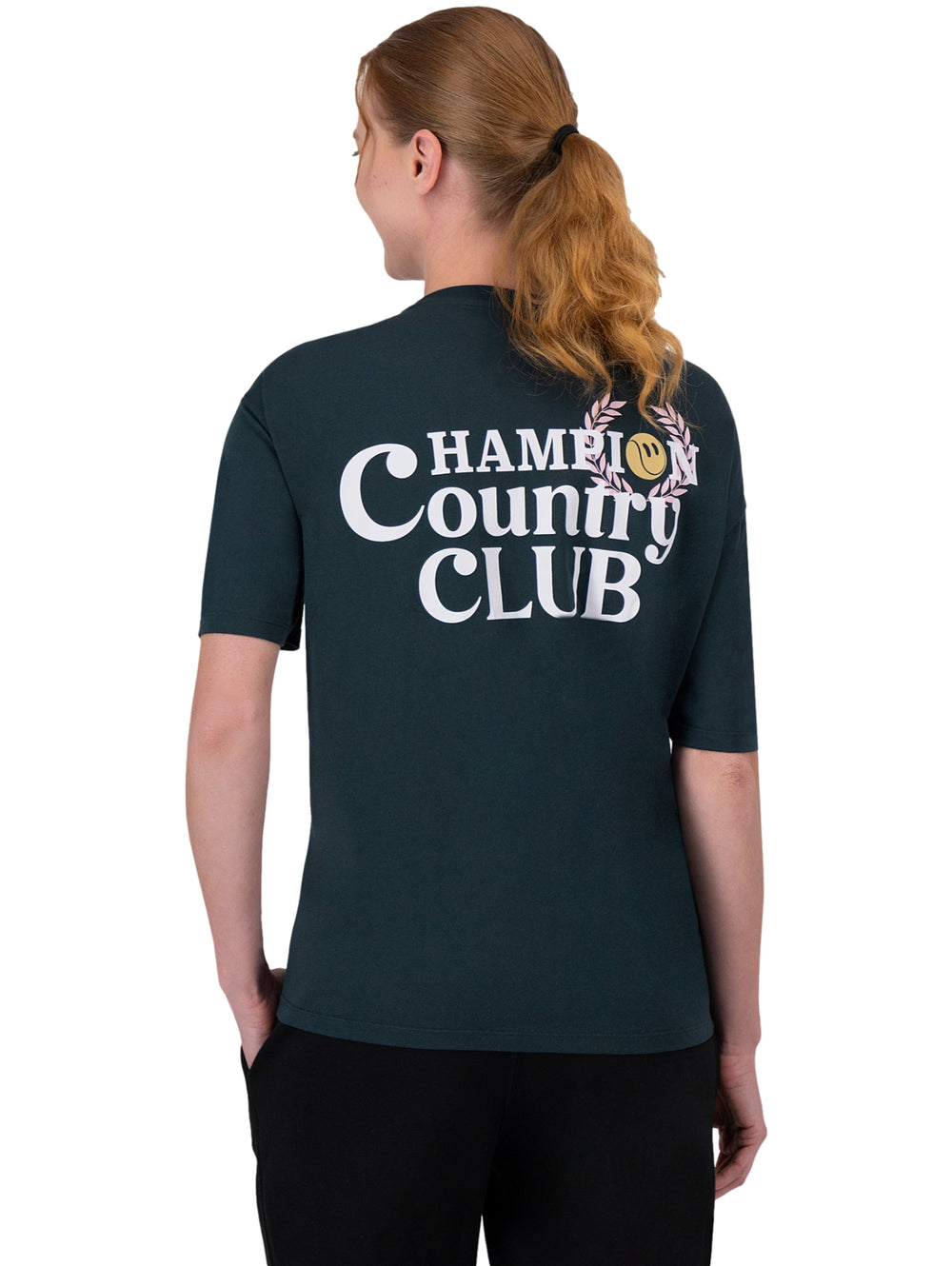 Mujer vistiendo una camiseta deportiva de color verde oscuro con logotipo de Champion en el pecho y manga.