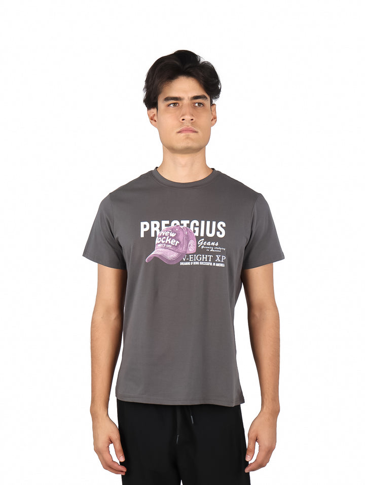 Hombre vistiendo playera gris de manga corta con estampado gráfico de una gorra rosa y texto en el pecho.