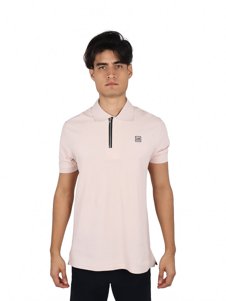 Hombre vistiendo playera polo color rosa claro con cierre en el cuello y un pequeño parche en el pecho.