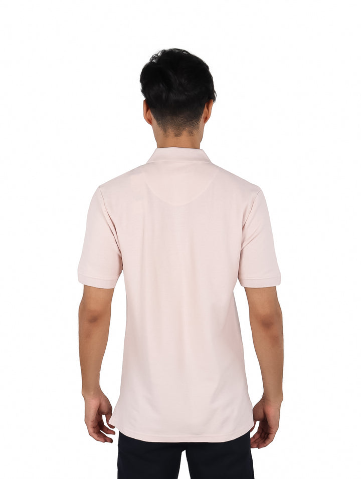 Hombre vistiendo playera polo color rosa claro con cierre en el cuello y un pequeño parche en el pecho.