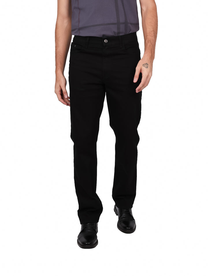 Hombre vistiendo pantalones jeans color negro de corte recto y zapatos negros sobre fondo blanco.