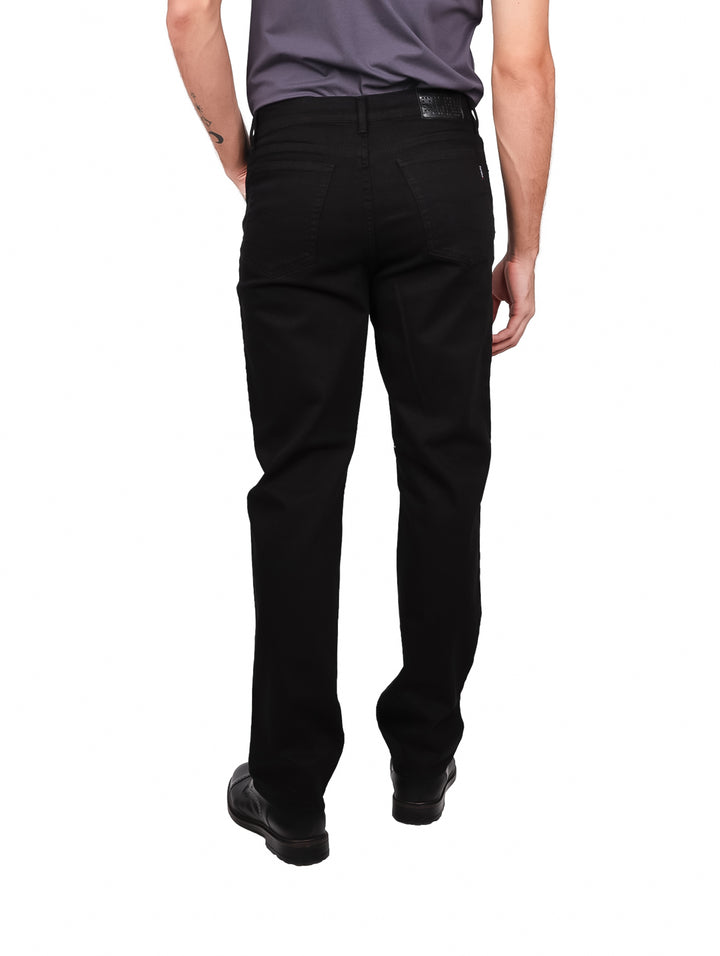 Hombre vistiendo pantalones jeans color negro de corte recto y zapatos negros sobre fondo blanco.