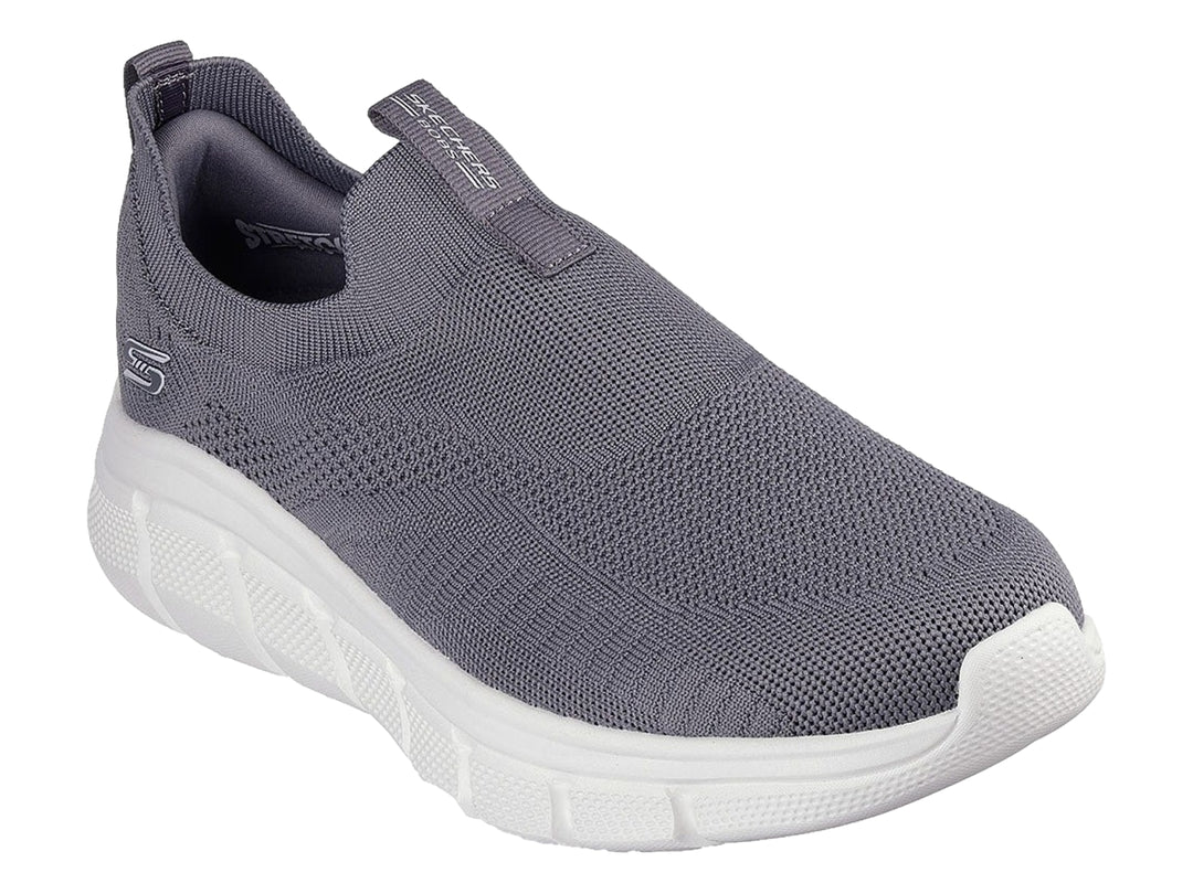 Tenis Skechers color gris oscuro con suela blanca, diseño slip-on de tejido flexible.