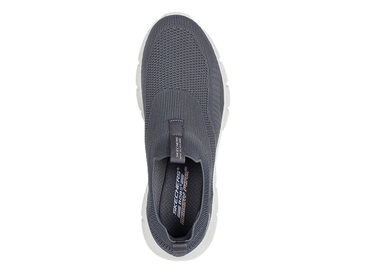 Tenis Skechers color gris oscuro con suela blanca, diseño slip-on de tejido flexible.
