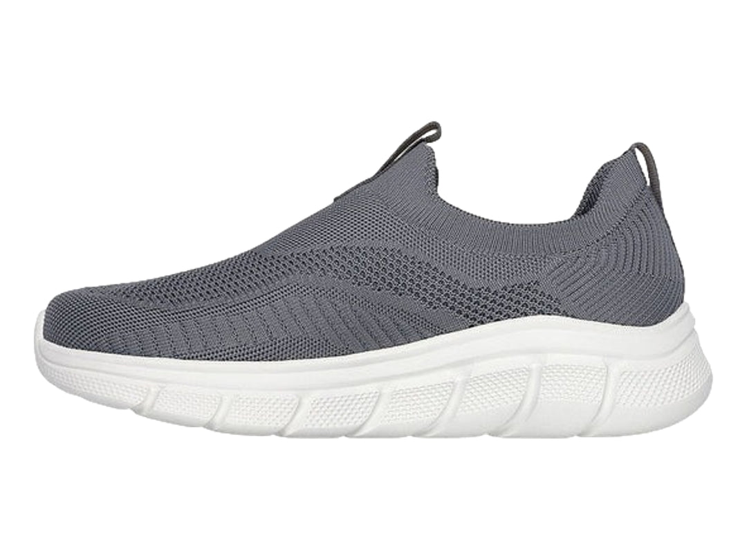 Tenis Skechers color gris oscuro con suela blanca, diseño slip-on de tejido flexible.