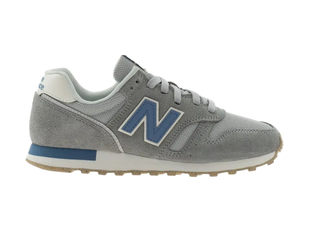Tenis New Balance color gris con detalles en azul y suela beige.