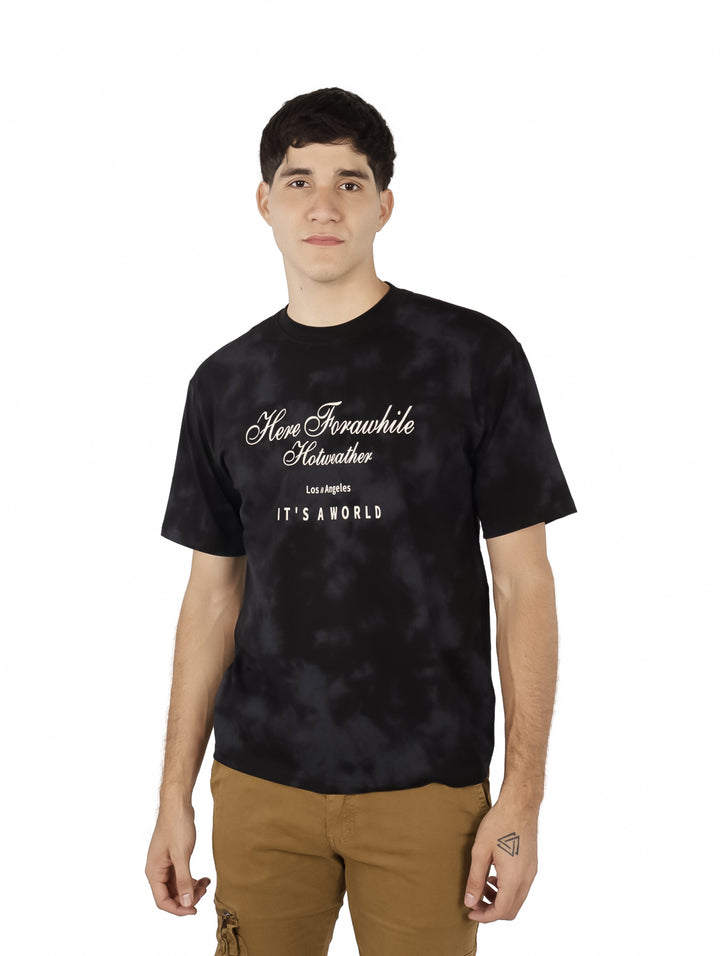 Hombre vistiendo playera oversize color negro con efecto tie-dye y estampado blanco en el pecho.
