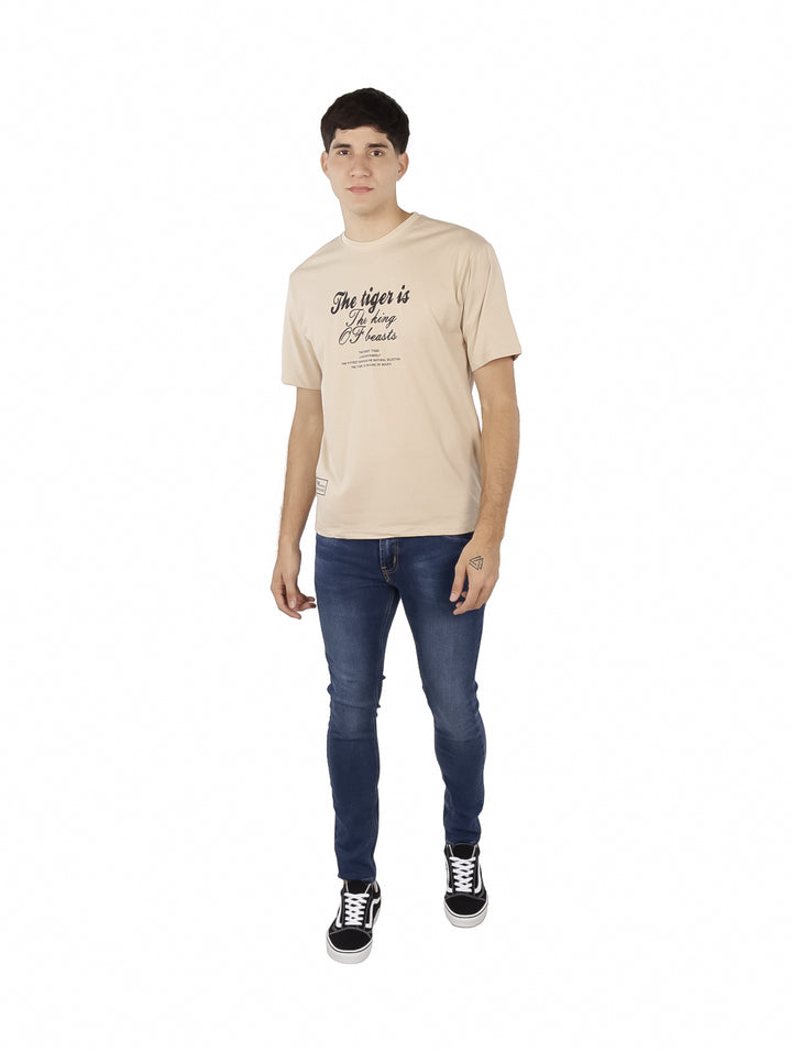 Hombre vistiendo playera oversize color khaki con estampado de texto en negro en el pecho.