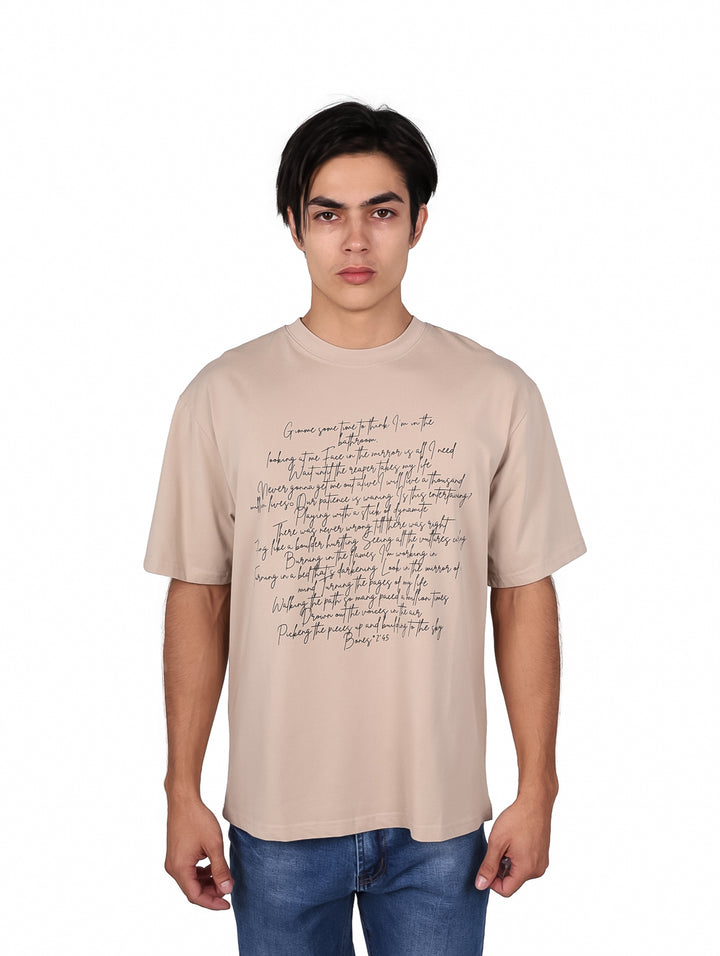 Hombre vistiendo playera oversize color khaki con texto impreso en la parte frontal.