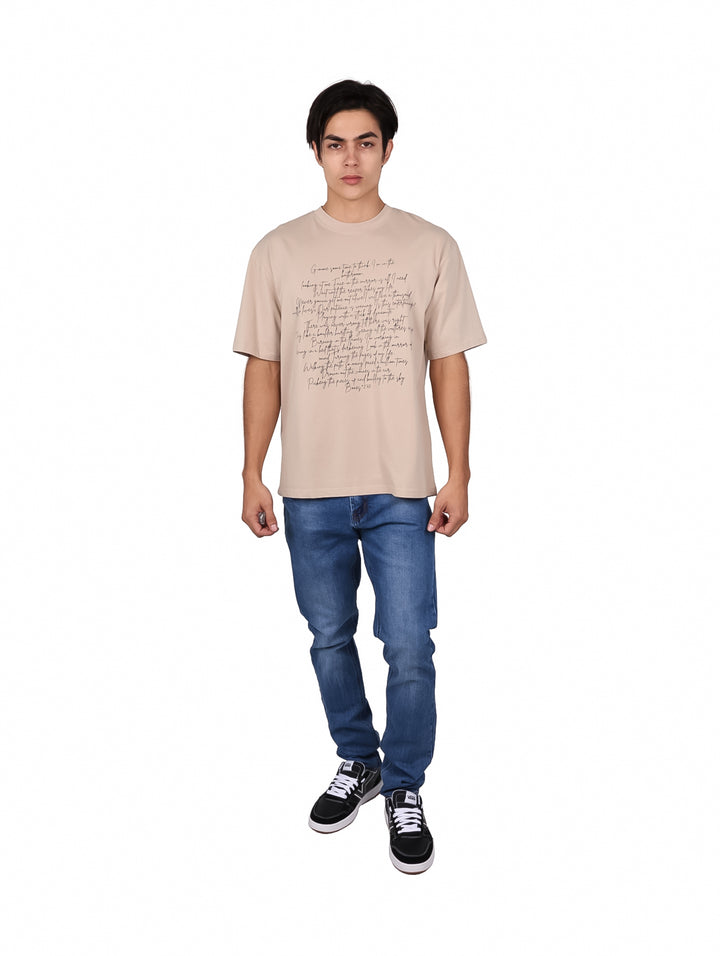 Hombre vistiendo playera oversize color khaki con texto impreso en la parte frontal.