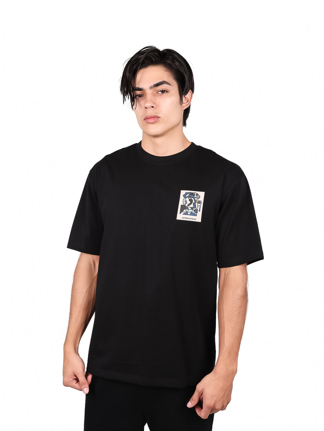 Hombre vistiendo playera negra de manga corta con un pequeño estampado cuadrado en el pecho.