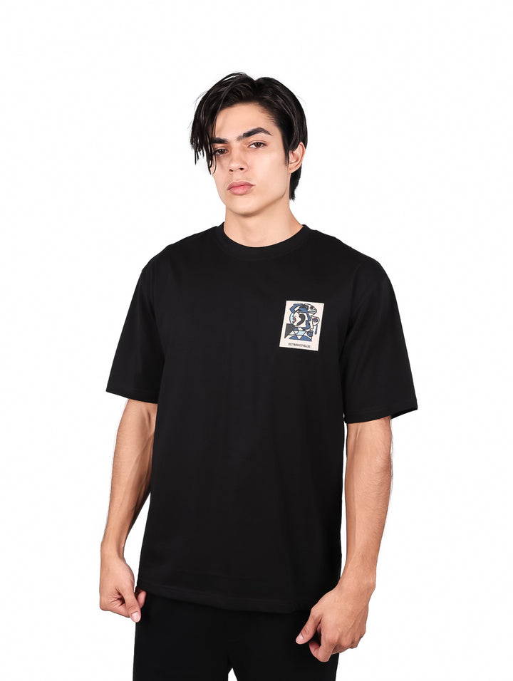 Hombre vistiendo playera negra de manga corta con un pequeño estampado cuadrado en el pecho.