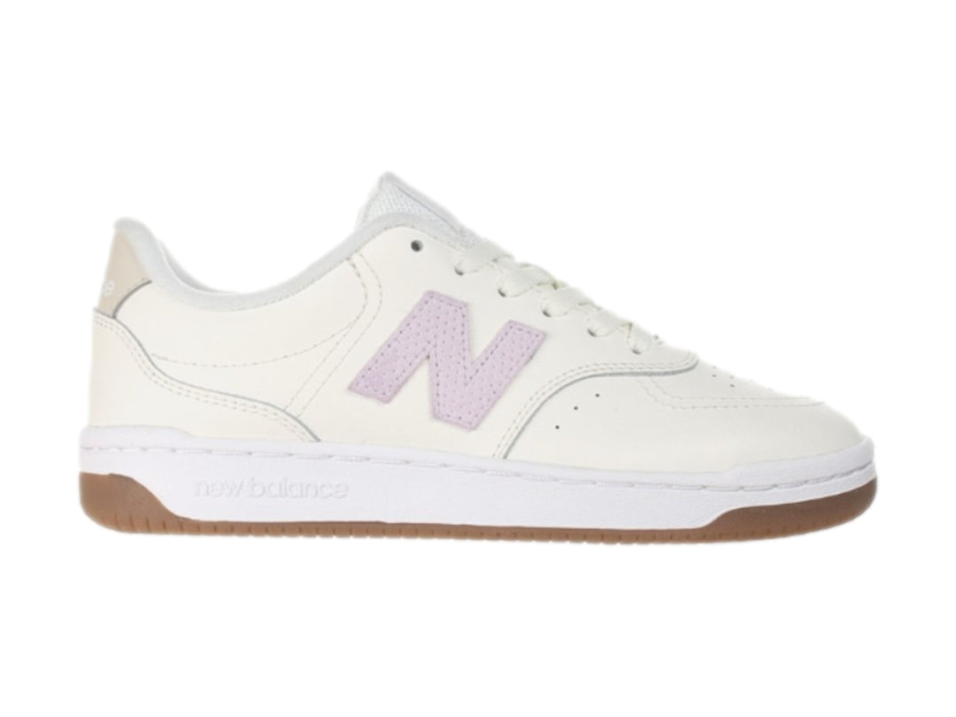 Tenis New Balance color blanco hueso con logotipo morado y suela color café.