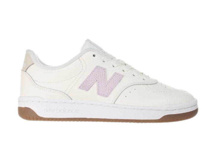Tenis New Balance color blanco hueso con logotipo morado y suela color café.