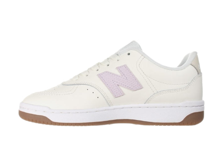 Tenis New Balance color blanco hueso con logotipo morado y suela color café.