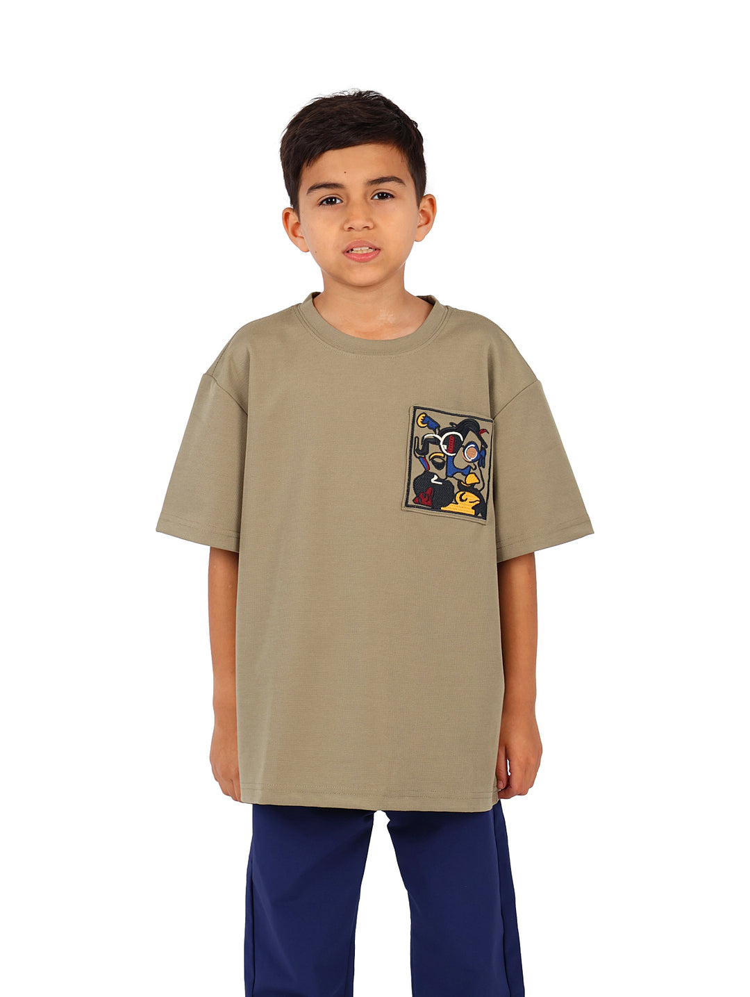 Niño vistiendo camiseta color verde militar con un estampado gráfico cuadrado en el pecho.