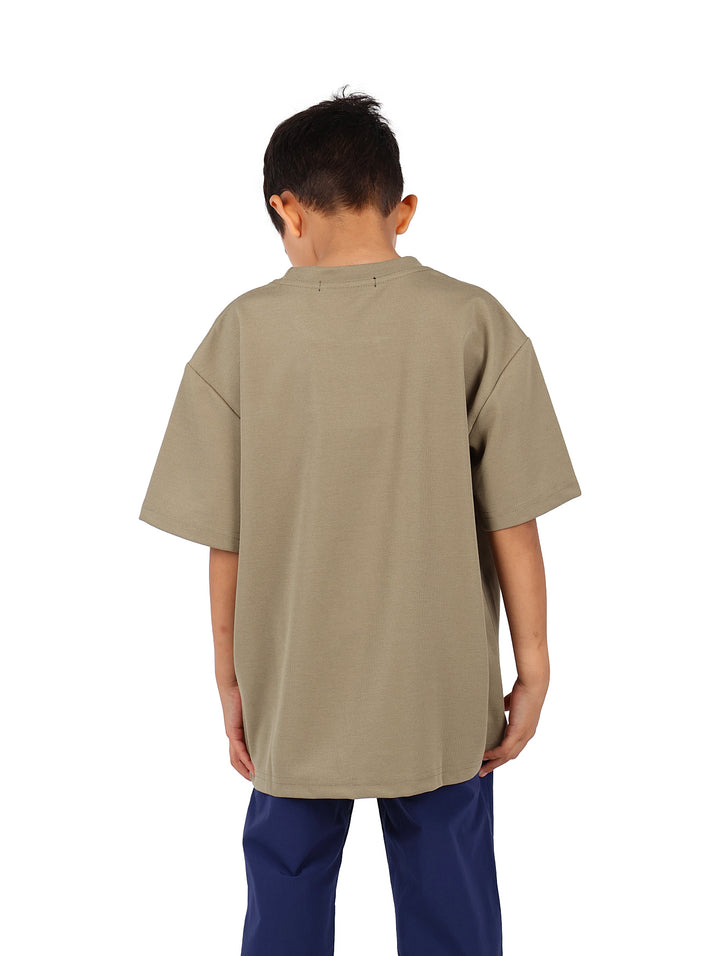 Niño vistiendo camiseta color verde militar con un estampado gráfico cuadrado en el pecho.