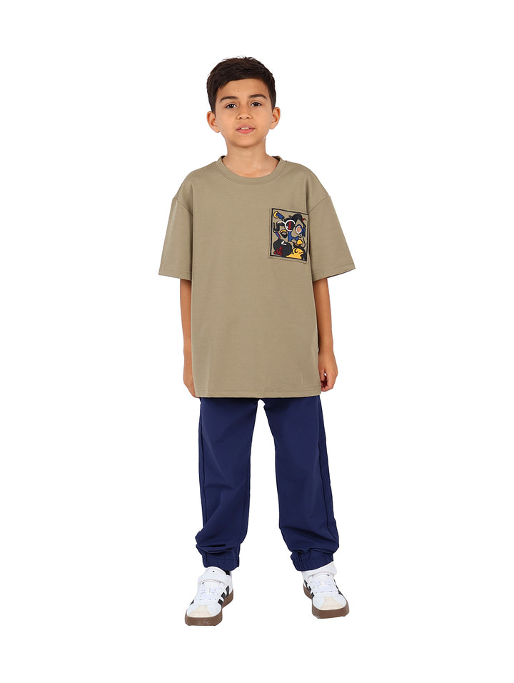 Niño vistiendo camiseta color verde militar con un estampado gráfico cuadrado en el pecho.