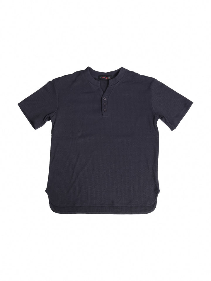 Conjunto de ropa para niño compuesto por camisa gris oscuro de manga corta y short a juego con tenis blancos.