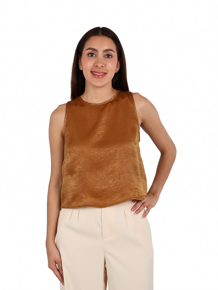 Mujer vistiendo una blusa sin mangas de color café brillante y pantalones beige.