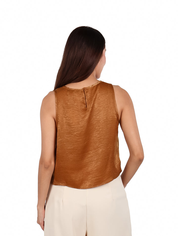 Mujer vistiendo una blusa sin mangas de color café brillante y pantalones beige.