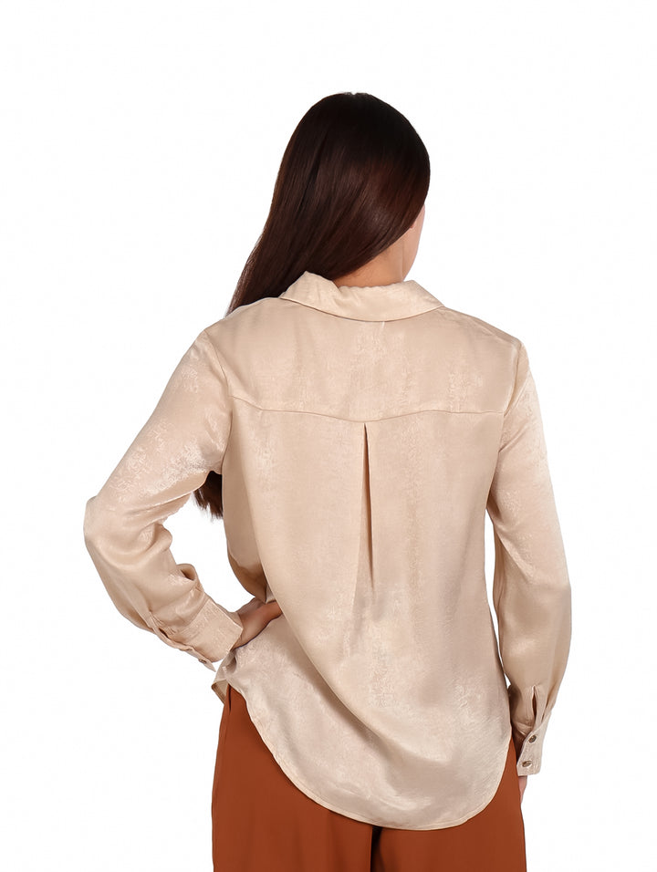 Mujer vistiendo una camisa beige de satín con botones y pantalones color café.