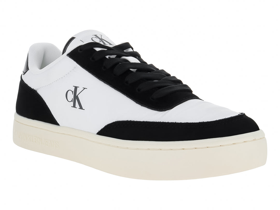 Tenis Calvin Klein de cuero color blanco con detalles en negro y suela plana blanca.