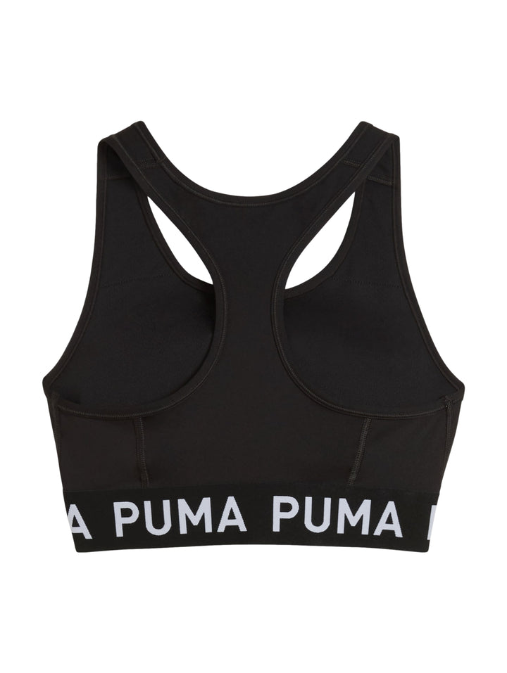 Mujer usando un bra deportivo negro de PUMA sosteniendo un balón medicinal.