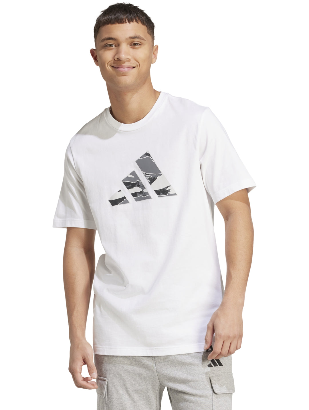 Hombre vistiendo playera blanca Adidas con logo gráfico camuflado en el pecho.