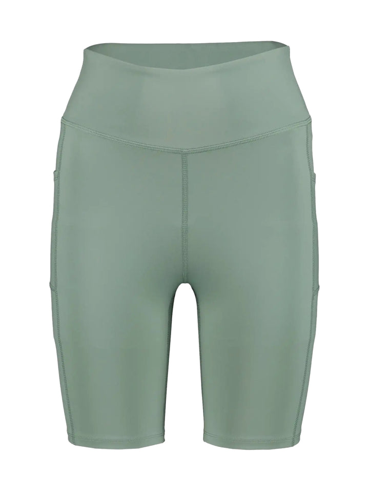 Mujer vistiendo biker shorts de color verde claro de cintura alta y calzado deportivo gris.