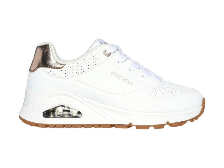 Tenis Skechers blancos para niña con detalles dorados en el talón y suela blanca con amortiguación visible.