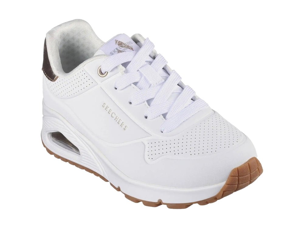 Tenis Skechers blancos para niña con detalles dorados en el talón y suela blanca con amortiguación visible.