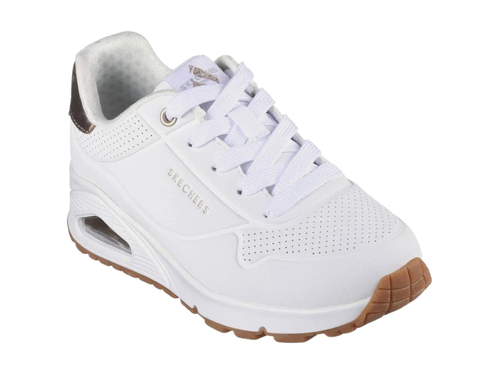 Tenis Skechers blancos para niña con detalles dorados en el talón y suela blanca con amortiguación visible.
