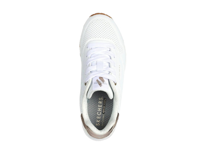 Tenis Skechers blancos para niña con detalles dorados en el talón y suela blanca con amortiguación visible.
