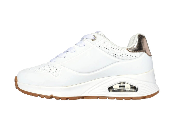 Tenis Skechers blancos para niña con detalles dorados en el talón y suela blanca con amortiguación visible.