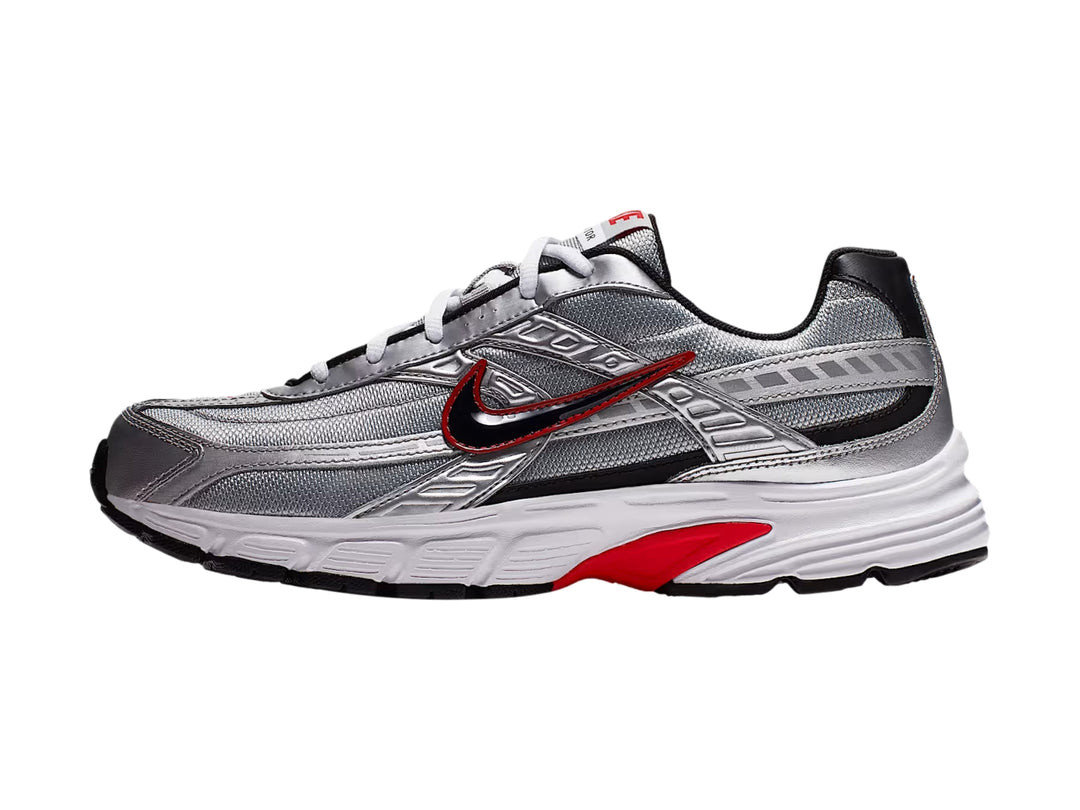 Tenis Nike Initiator en color plata metálico con detalles en rojo y negro y suela blanca.