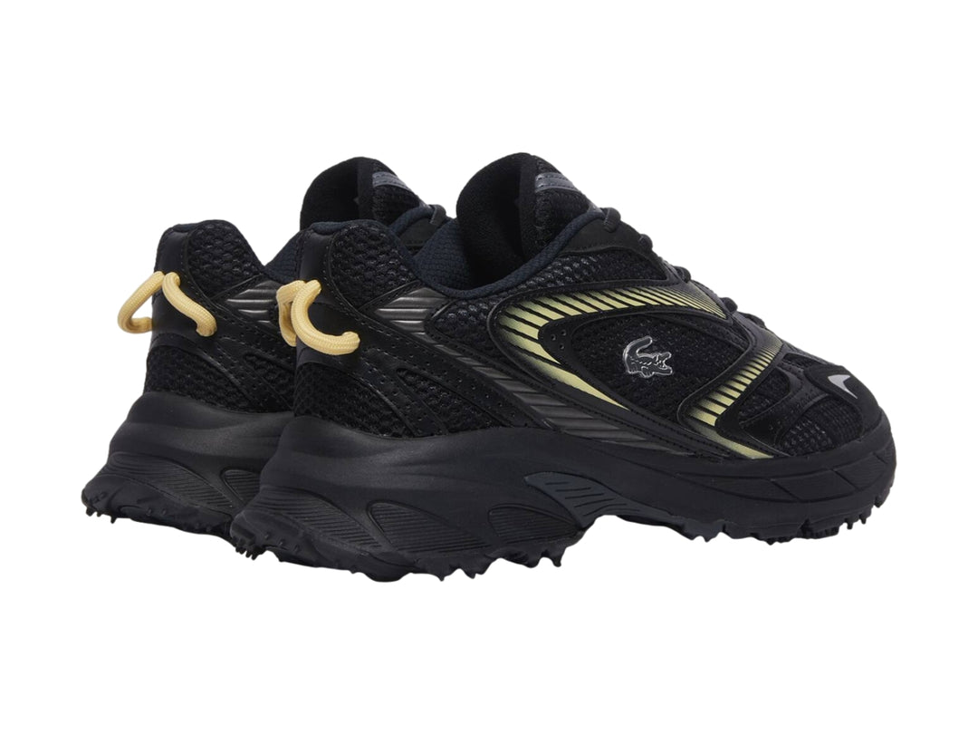 Tenis deportivos Lacoste color negro con detalles en amarillo y suela gruesa.
