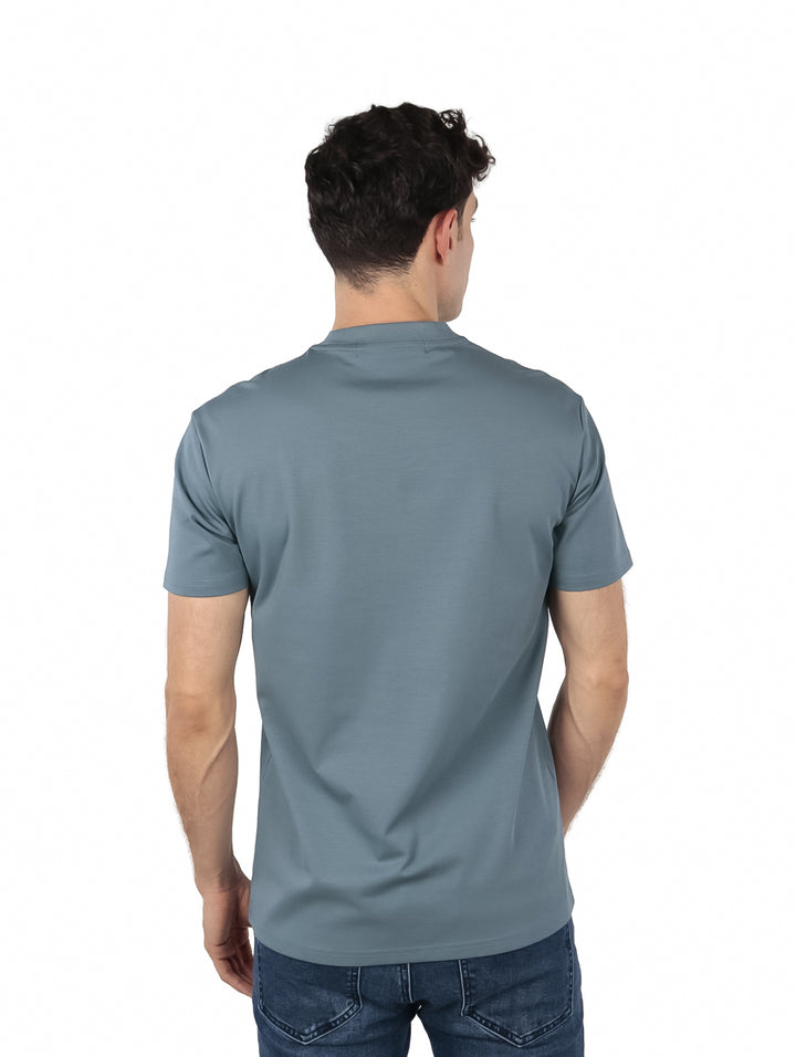 Hombre vistiendo playera color teal con estampado decorativo blanco y verde alrededor del cuello.