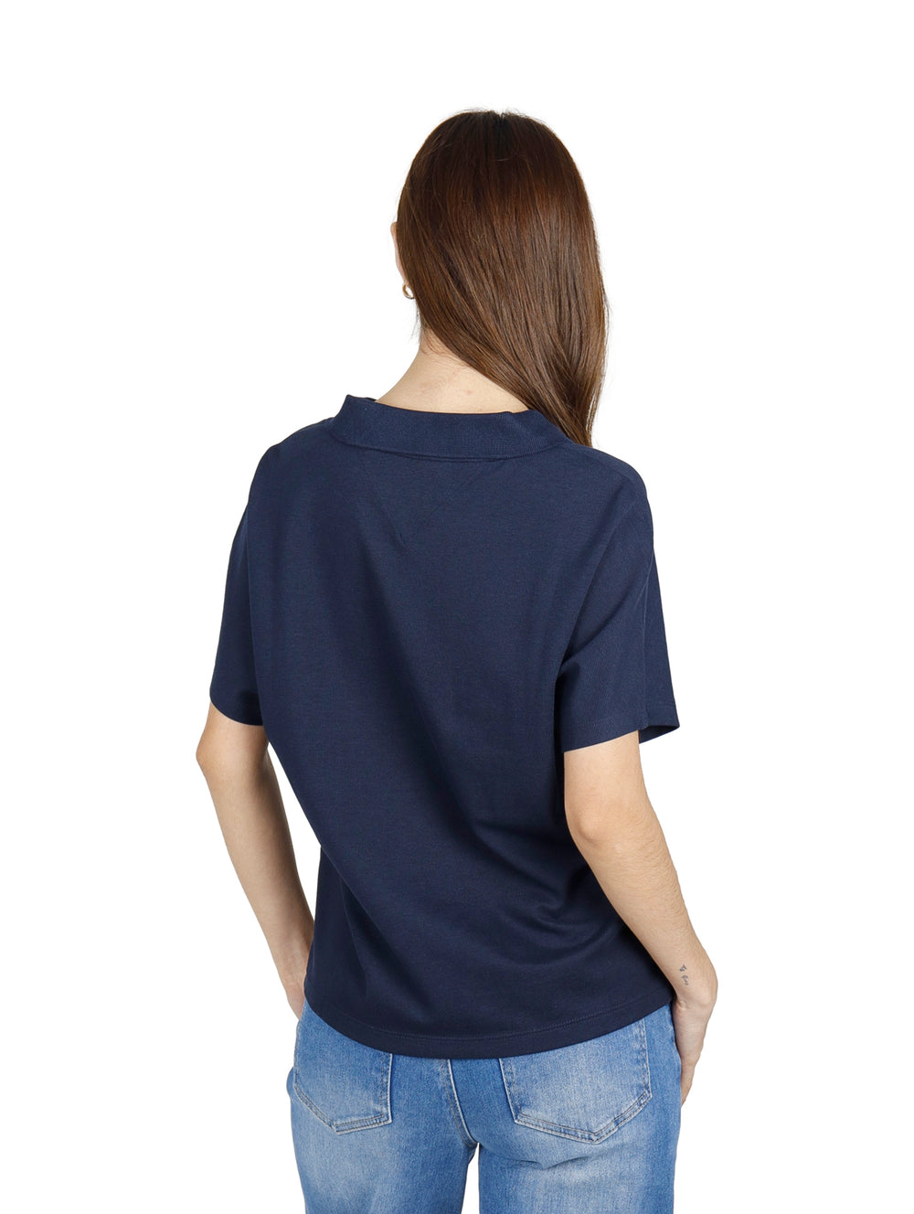 Mujer vistiendo polo Tommy Hilfiger color azul marino con detalles rojos y blancos en el cuello y jeans azules.