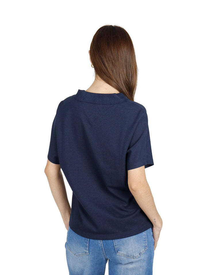 Mujer vistiendo polo Tommy Hilfiger color azul marino con detalles rojos y blancos en el cuello y jeans azules.
