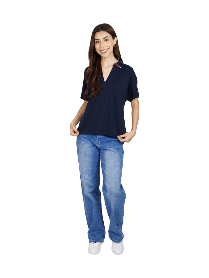 Mujer vistiendo polo Tommy Hilfiger color azul marino con detalles rojos y blancos en el cuello y jeans azules.
