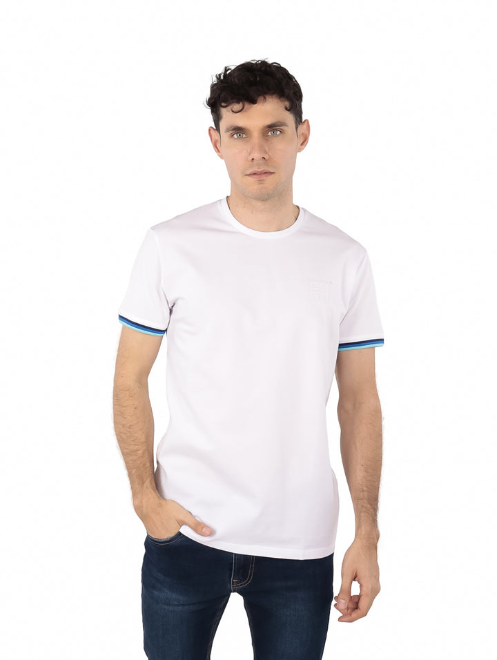 Hombre vistiendo playera blanca de manga corta con rayas en las mangas y pantalones azules.